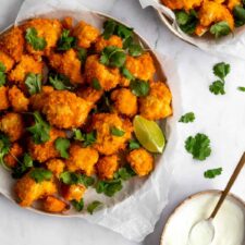 a plate and a bowl with cauliflower bites and coriander leaves on top and a small bowl with white cream dressing on the side
