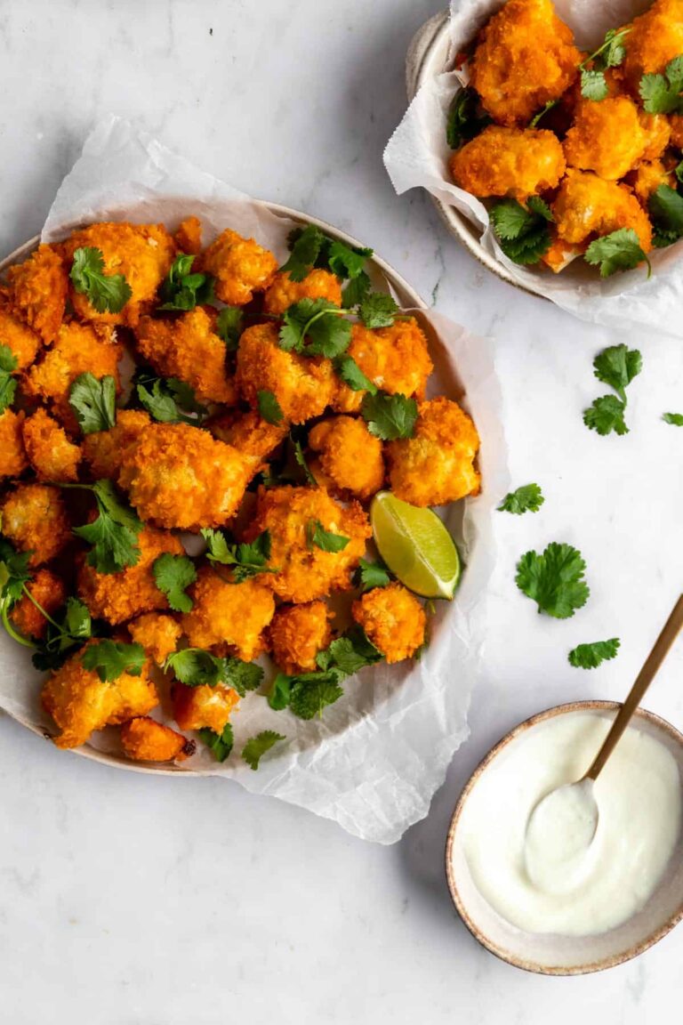 a plate and a bowl with cauliflower bites and coriander leaves on top and a small bowl with white cream dressing on the side