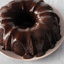 a bundt chocolate cake with chocolate glaze on top on a pink plate on top of a marble table