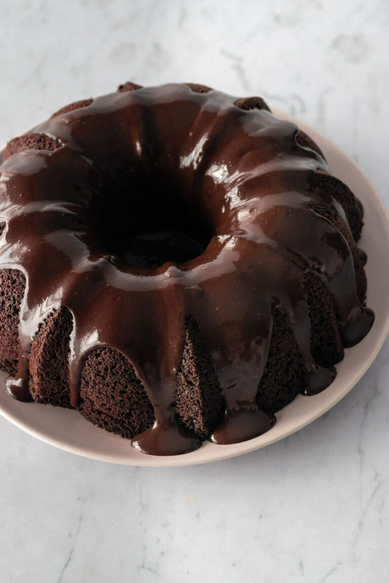 a bundt chocolate cake with chocolate glaze on top on a pink plate on top of a marble table
