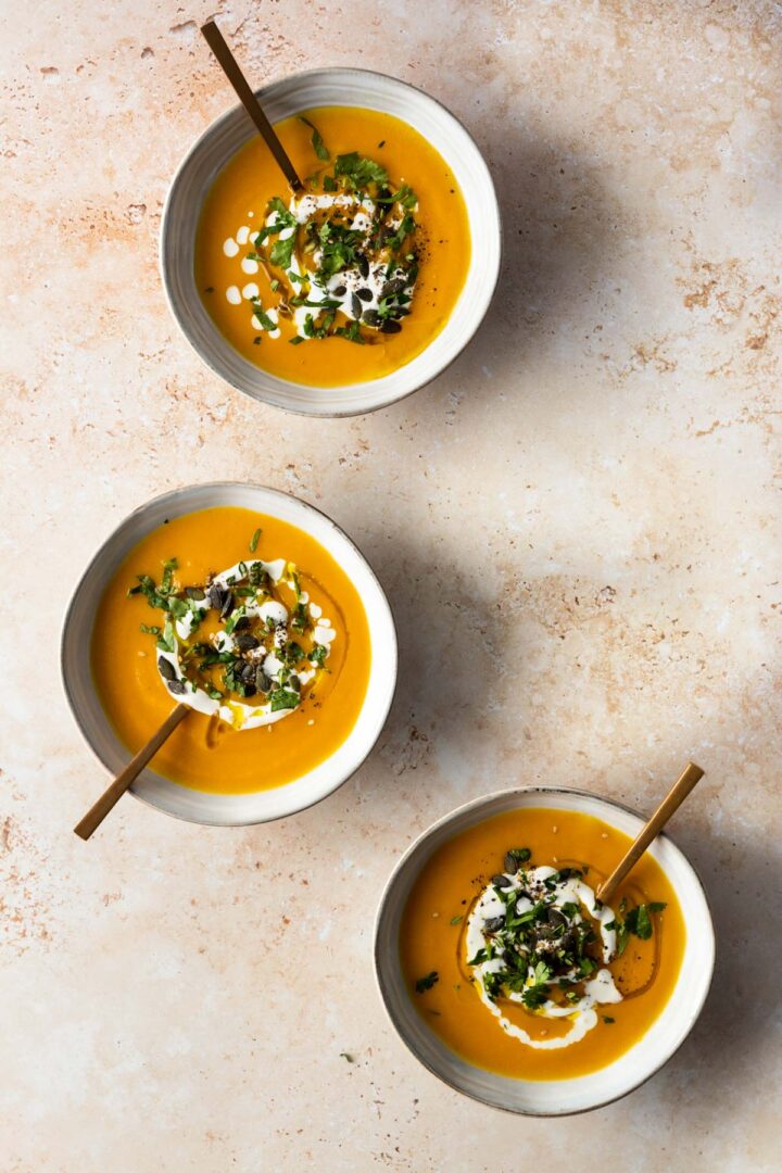 three bowls with soup, a drizzle of coconut milk, pumpkin seeds, a drizzle of olive oil and chopped coriander on top