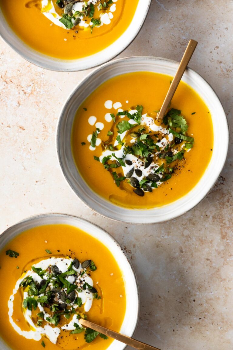 three bowls with soup, a drizzle of coconut milk, pumpkin seeds, a drizzle of olive oil and chopped coriander on top
