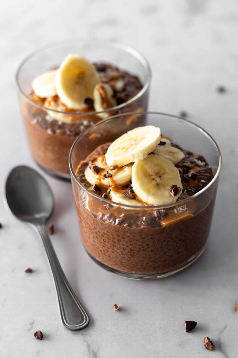 two glass bowls with chocolate chia pudding, sliced banana, cacao nibs, peanut butter and a spoon on the side