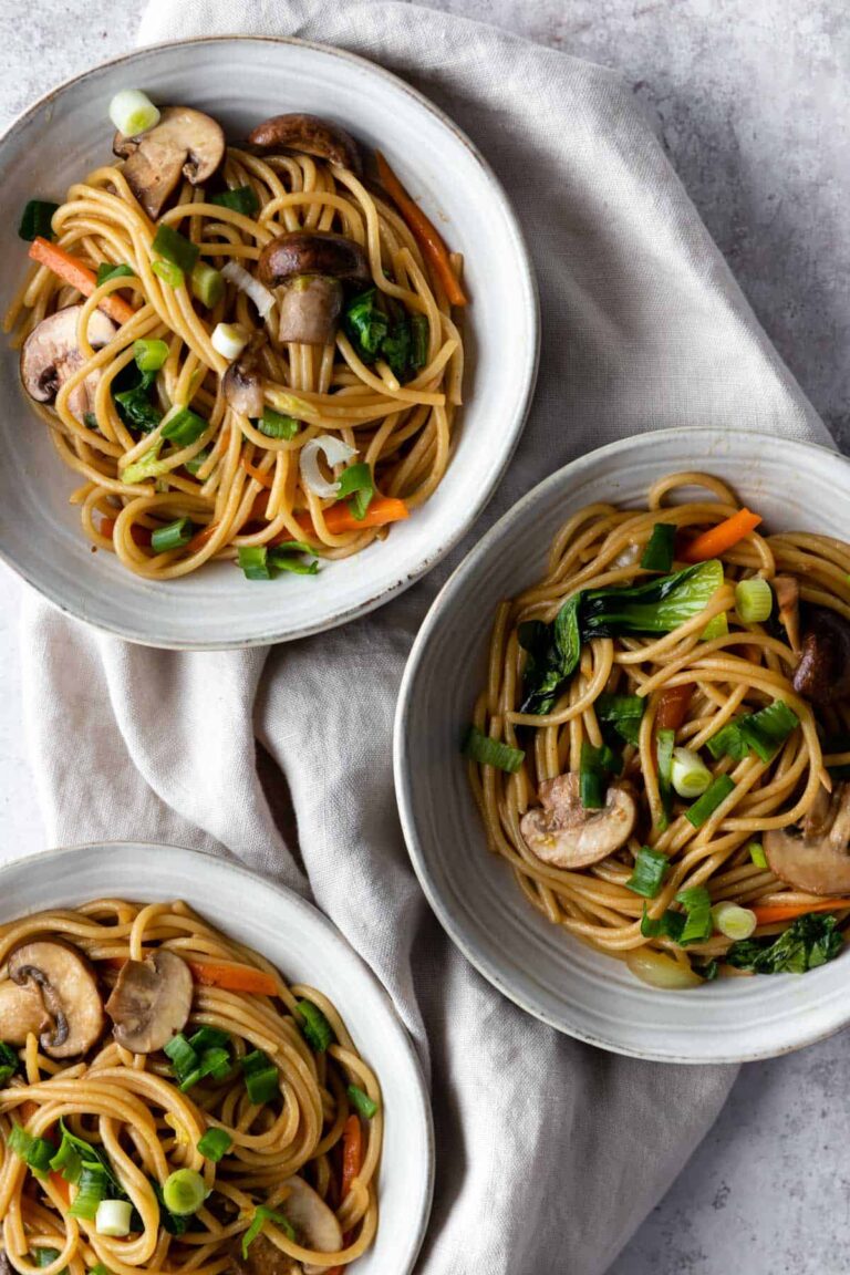 three bowls with noodles, sliced mushrooms, chopped cabbage, julienned carrots and chopped green onions on top of a beige kitchen towel