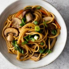 a bowl with noodles, sliced mushrooms, chopped cabbage, julienned carrots and chopped green onions