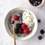 a bowl with chia pudding, coconut chips, berries, a spoon and a small bowl with berries on the side