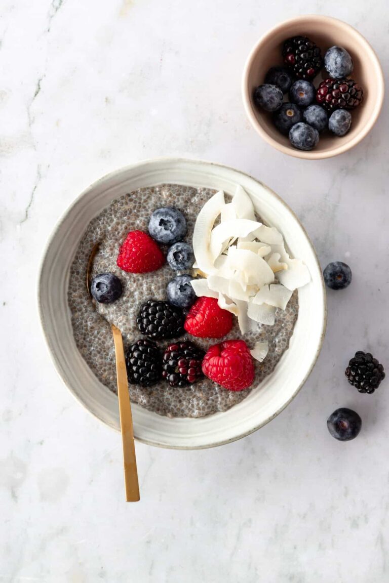 a bowl with chia pudding, coconut chips, berries, a spoon and a small bowl with berries on the side