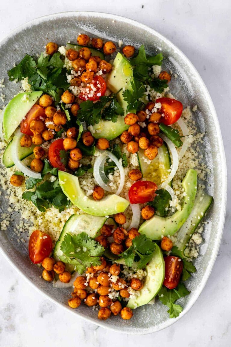 close up of a plate with couscous, sliced avocado, sliced cucumber, cherry tomatoes, roasted chickpeas, sliced onion and coriander