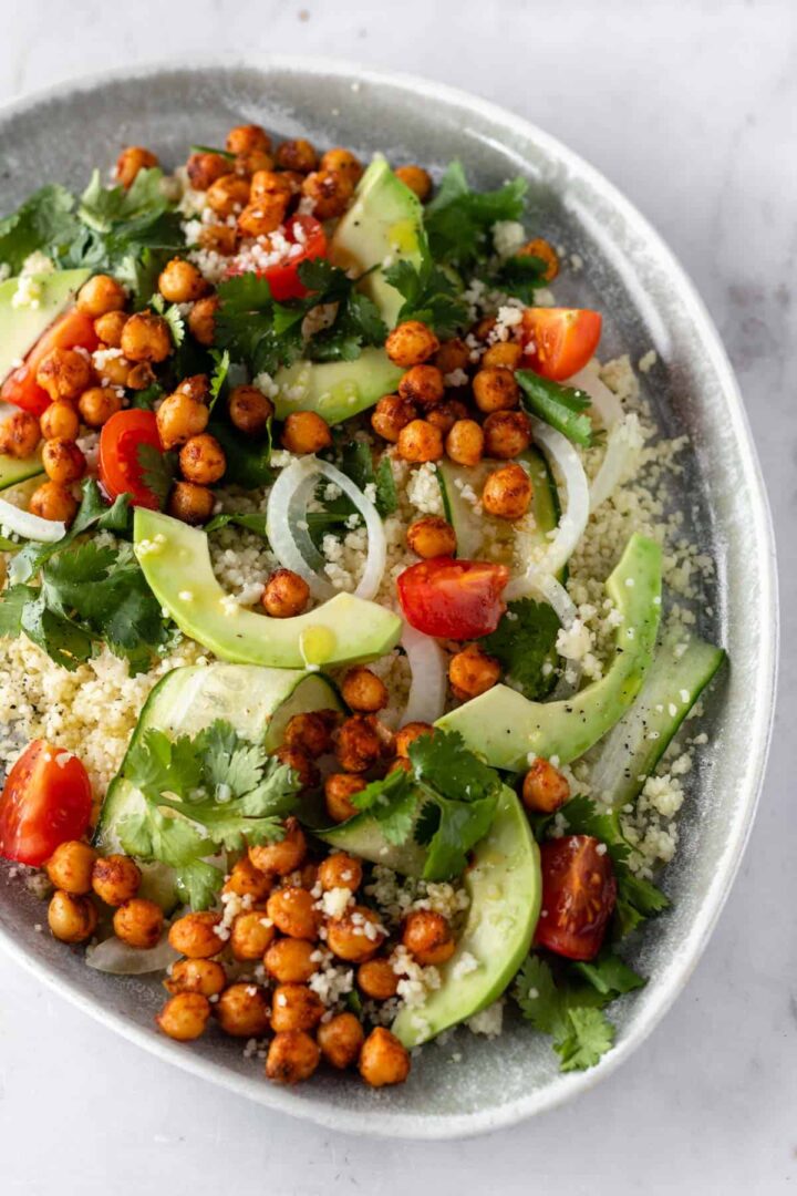 a plate with couscous, sliced avocado, sliced cucumber, cherry tomatoes, roasted chickpeas, sliced onion and coriander
