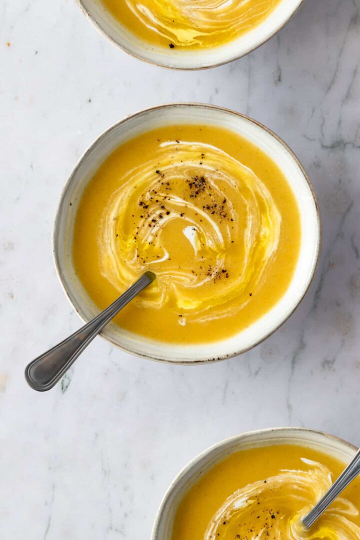 close up bowls with zucchini soup with a drizzle of coconut milk and black pepper on top
