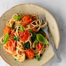 a plate with spaghetti, cherry tomatoes, spinach, basil leaves and a fork on the side