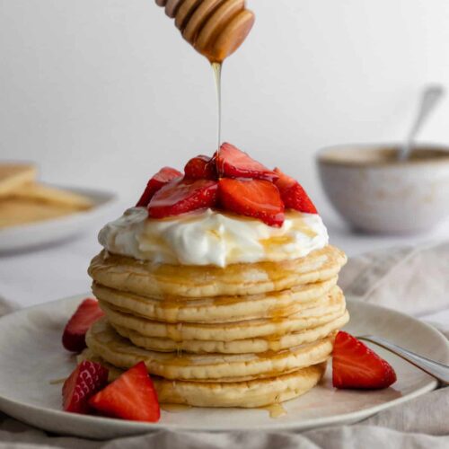 a plate with a stack of vegan pancakes with coconut yogurt, strawberries and maple syrup on top
