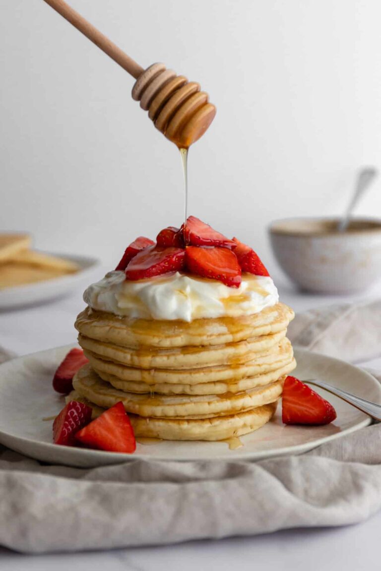 a plate with a stack of vegan pancakes with coconut yogurt, strawberries and maple syrup on top