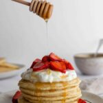 pancake stack with, strawberries, maple syrup and coconut yogurt on top