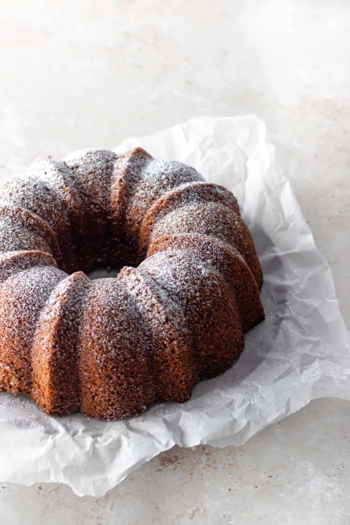 a bundt carrot cake with powdered sugar on top, on top of white parchment paper on a beige board