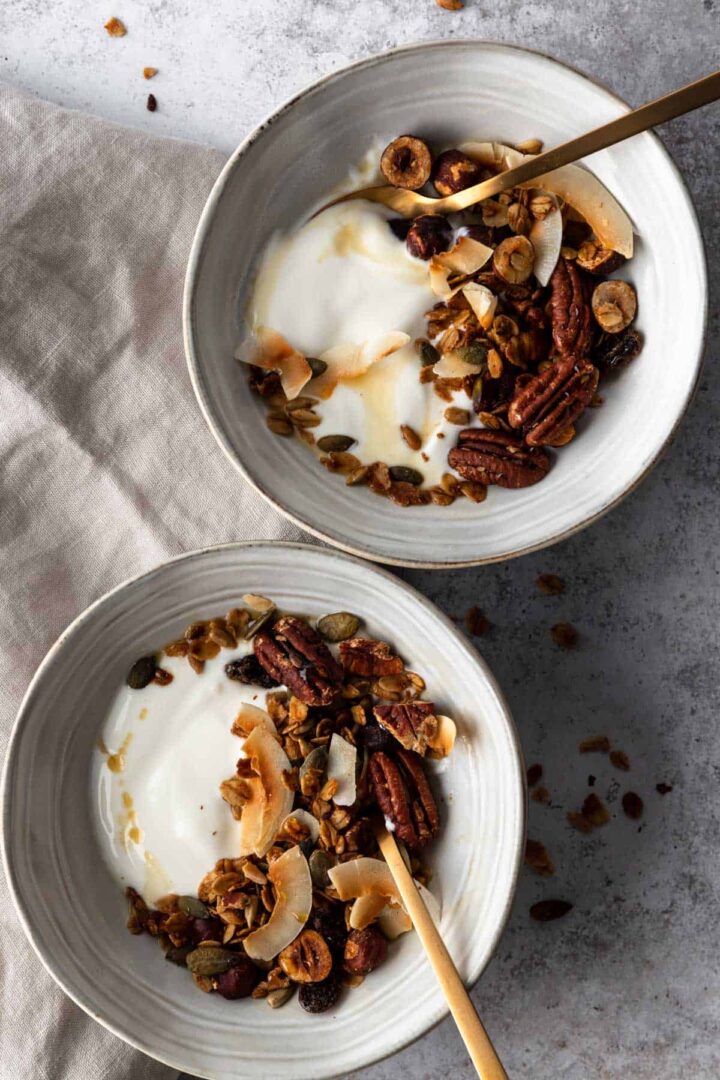 two bowls with granola, coconut yogurt and maple syrup on top