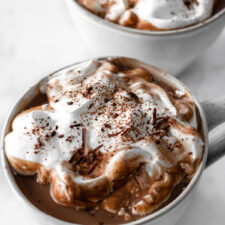 two mugs with hot chocolate with a vegan whipped cream and shredded chocolate on top