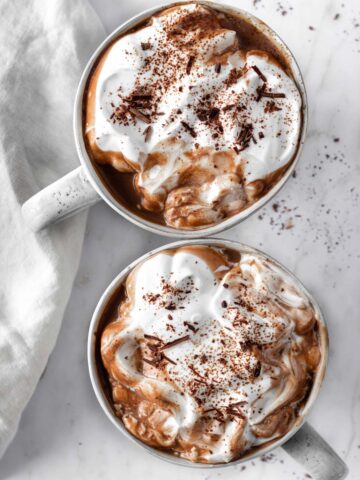 two mugs with hot chocolate with a vegan whipped cream and shredded chocolate on top