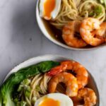 two ramen bowls with noodles, shrimp, boiled egg, green onions and bok choy