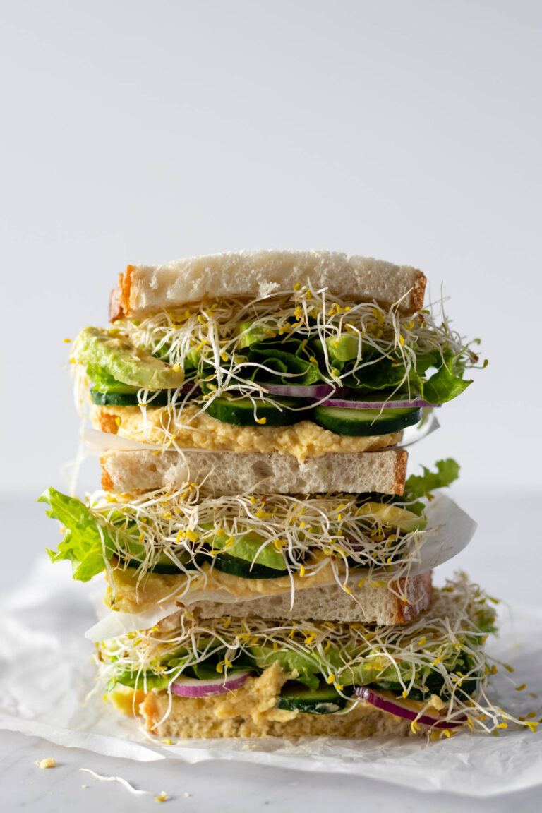 hummus sandwiches with avocado, red onion, cucumber, lettuce and micro greens on top of parchment paper
