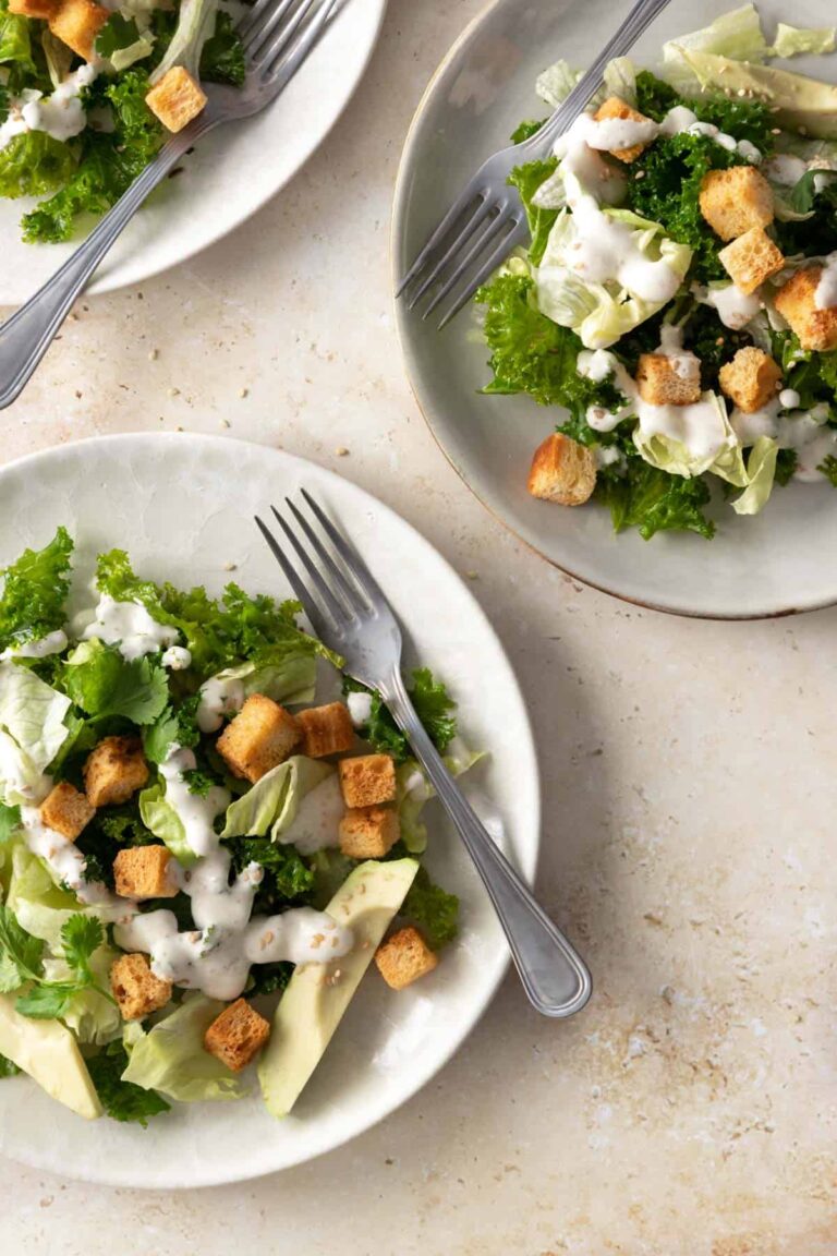three plates served with iceberg lettuce, sliced avocado, kale, bread croutons, white dressing and sesame seeds on top