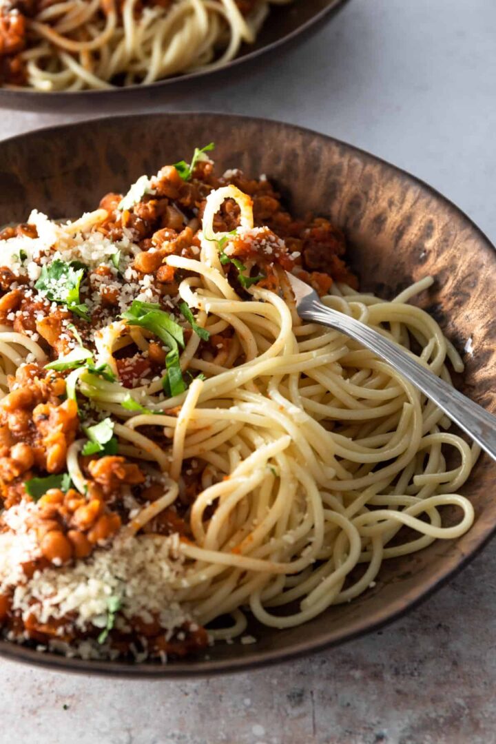 close up bowl with spaghetti, lentil and tomato sauce, grated parmesan and coriander. A small bowl with coriander on the side