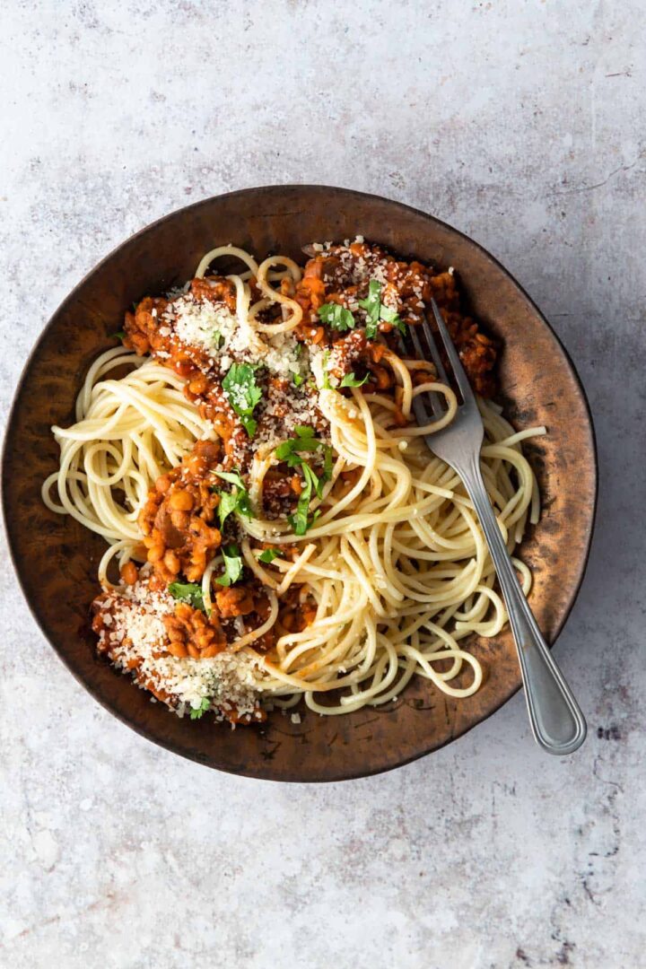 bowl with spaghetti, lentil and tomato sauce, grated parmesan and coriander. A small bowl with coriander on the side