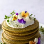 a plate with a stack of pancakes, coconut yogurt, edible flowers and match powder on top