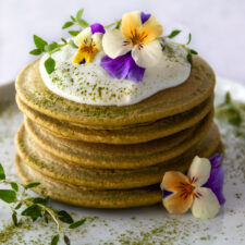 a plate with a stack of pancakes, coconut yogurt, edible flowers and match powder on top