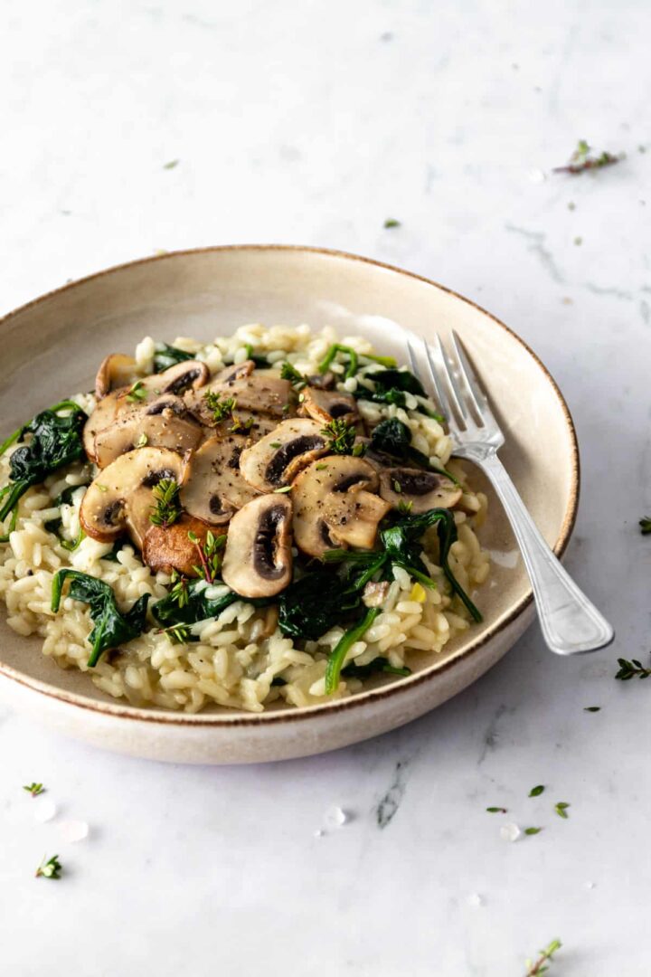 a plate with mushroom risotto with spinach, garnished with thyme and a fork on the side