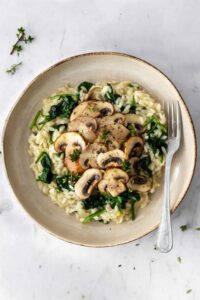 a plate with mushroom risotto with spinach, garnished with thyme and a fork on the side