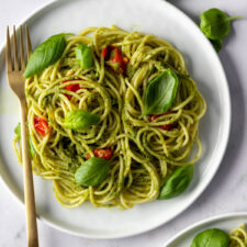 two plates with pesto spaghetti, cherry tomatoes and basil leaves