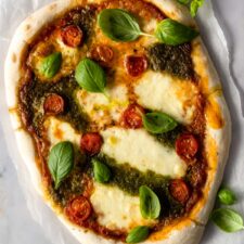 pizza with mozzarella, tomato sauce, pesto sauce, cherry tomatoes and basil leaves