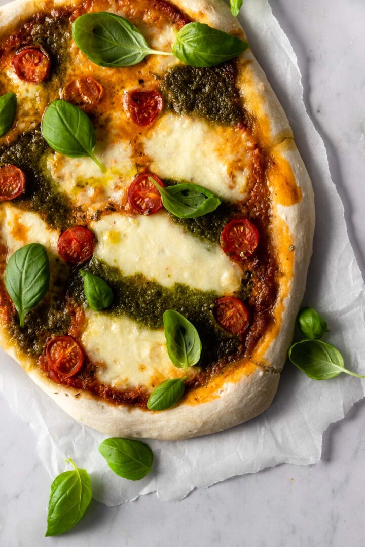 pizza on top of parchment paper with mozzarella, tomato sauce, pesto sauce, cherry tomatoes and basil leaves
