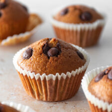 one muffin with chocolate chips and four muffins out of focus