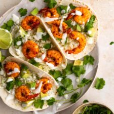 three shrimp tacos served on a plate and garnished with coriander and cream and a small bowl with more coriander leaves