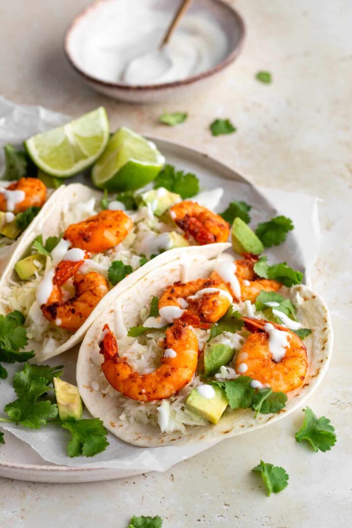 shrimps, cubbed avocado, and shredded cabbage served on top of tortillas and topped with coriander leaves and cream, with two lime wedges on the side