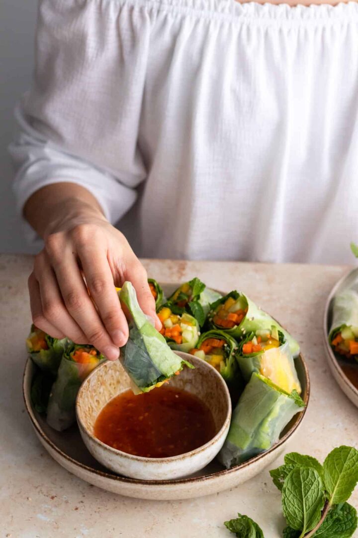 Rita holding a spring roll close a bowl with sweet chili sauce