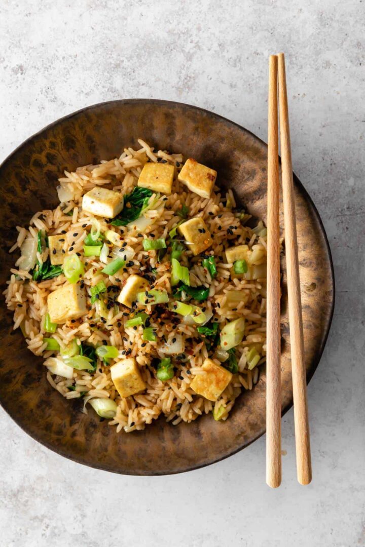 one bowl with cubed tofu, rice, cabbage, green onions, sesame seeds, chili flakes and chopsticks on the side