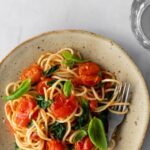 a plate with spaghetti, cherry tomatoes, spinach, basil leaves and a fork on the side
