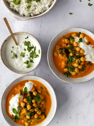 two bowls with chickpea curry, coconut yogurt and chopped coriander on top, another bowl with coconut yogurt and chopped coriander, a bowl with rice and chopped coriander