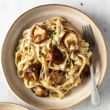 Shiitake mushrooms and fettuccine pasta served on a plate with fresh thyme on top