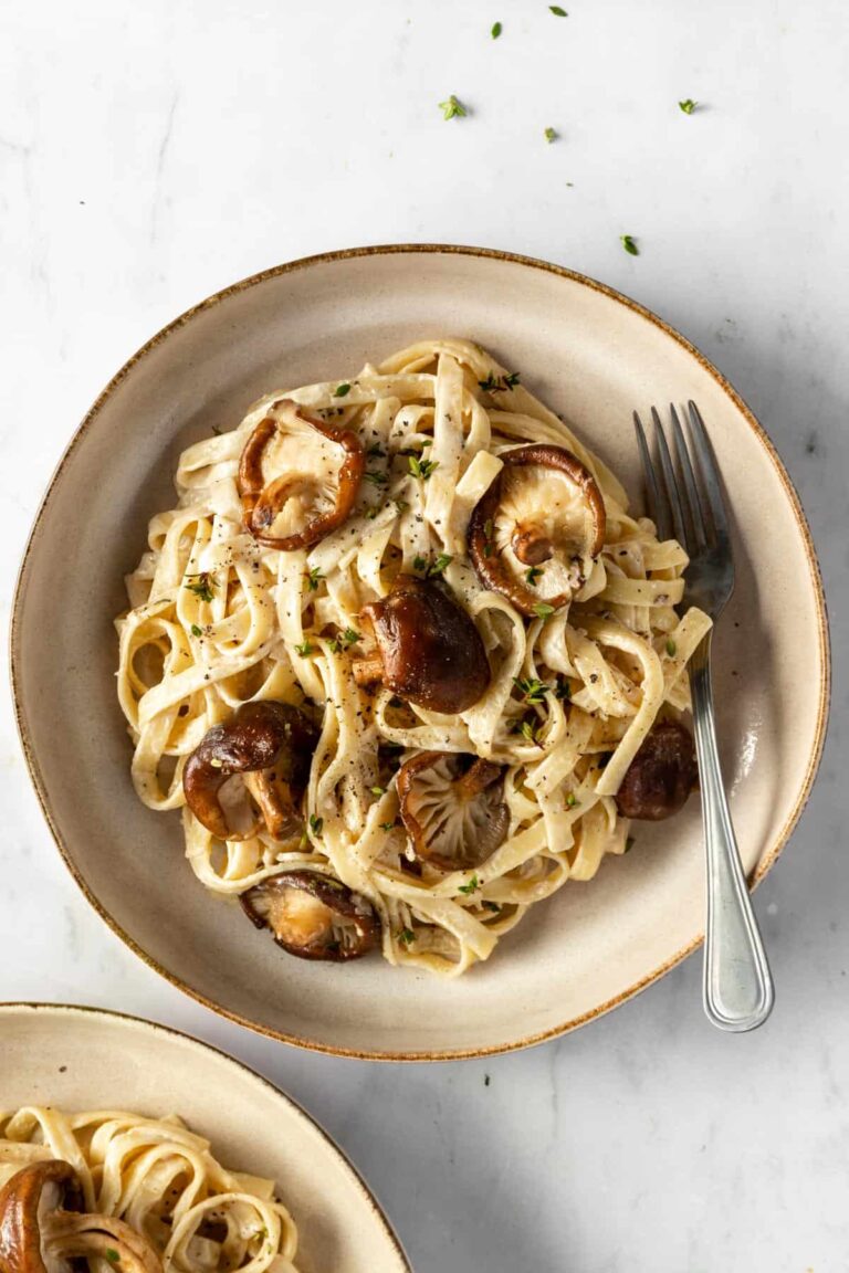 Shiitake mushrooms and fettuccine pasta served on a plate with fresh thyme on top