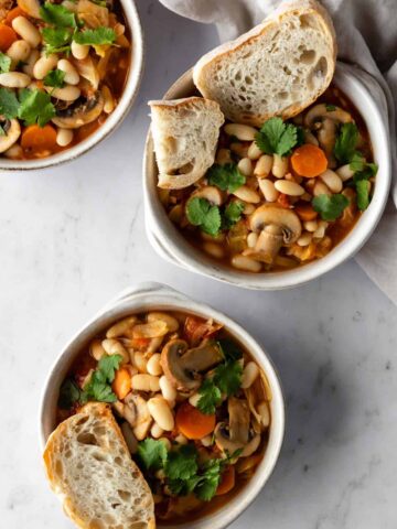 three bowls with white bean and mushroom stew, garnished with coriander and sliced toast bread on the side
