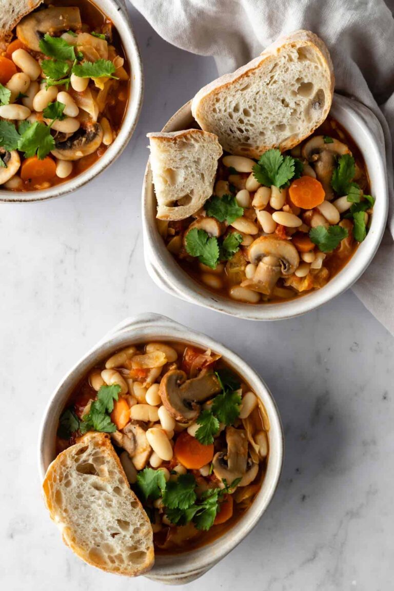 three bowls with white bean and mushroom stew, garnished with coriander and sliced toast bread on the side