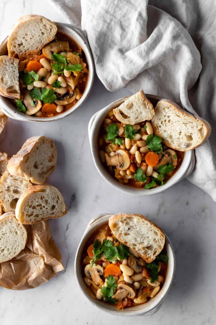 three bowls with white bean and mushroom stew, garnished with coriander and sliced toast bread on the side