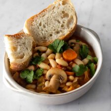 a bowl with beans, sliced mushrooms, sliced carrots, coriander and sliced bread on the side