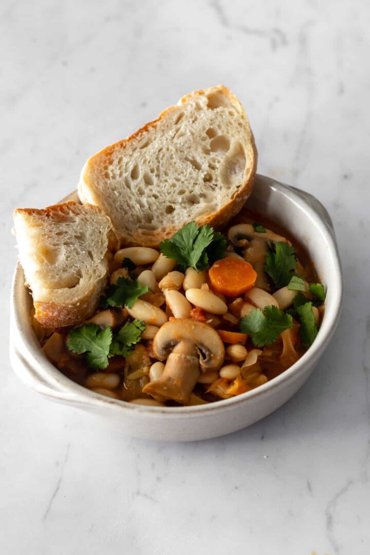 a bowl with beans, sliced mushrooms, sliced carrots, coriander and sliced bread on the side
