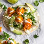 cauliflower tacos on top of parchment paper, garnished with coriander, lime wedges and cream sauce