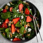 a grey bowl with spinach leaves, sliced strawberries, crumbled feta cheese and walnuts